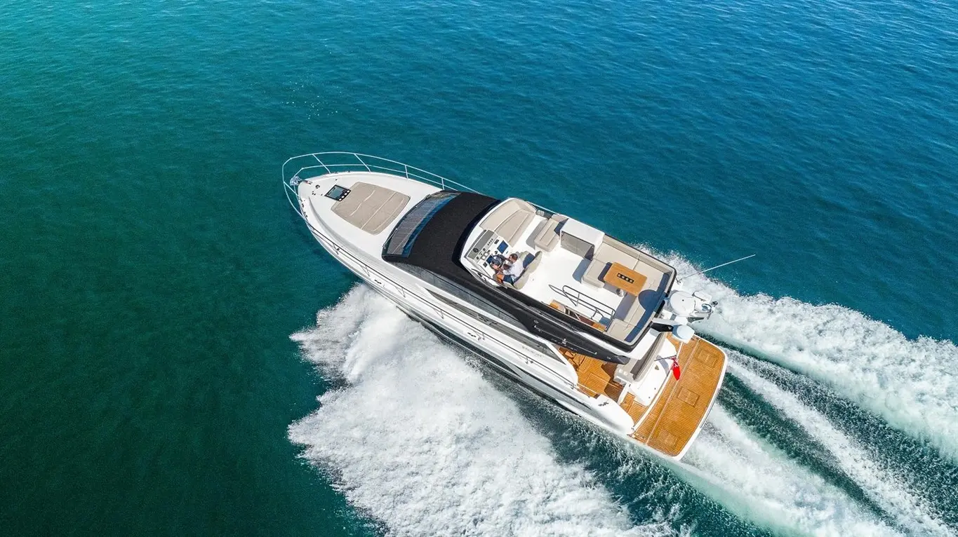 Luxury motor yacht cruising through clear blue waters, creating white wake trails behind.
